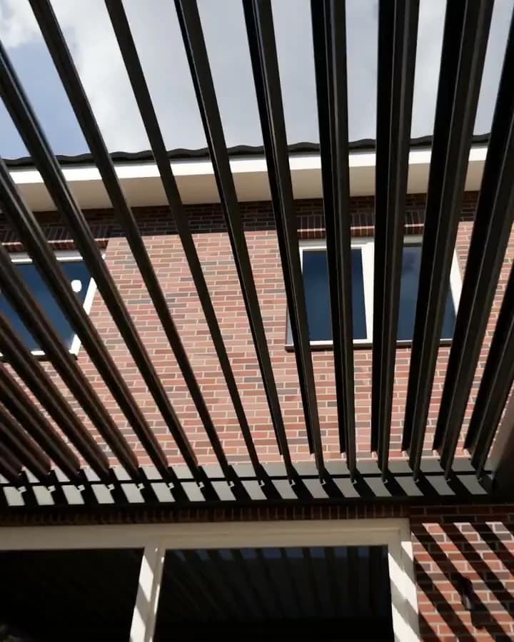 Lamellendak in antraciet aan een bakstenen huis, van onderaf, met de schaduw van de lamellen op de gevel